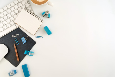 Flat lay, top view office table desk. Work space with blank note book, keyboard, blue office supplies and coffee cup on white background.の写真素材
