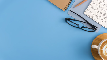 Flat lay, top view office table desk. Workspace with blank note book, keyboard, office supplies and coffee cup on light blue background.の写真素材