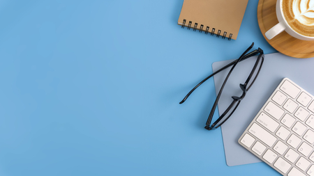 Flat lay, top view office table desk. Workspace with blank note book, keyboard, office supplies and coffee cup on light blue background.の写真素材