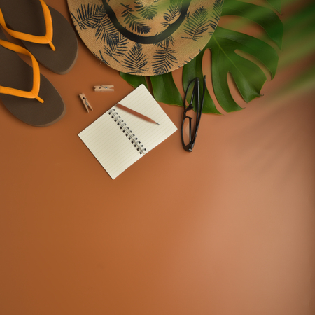 Flat lay, top view workspace with eye glasses, notebook, hat, pencil, green leaf, shoes and coffee cup on brown background. Summer stylish traveller blogger concept.の写真素材