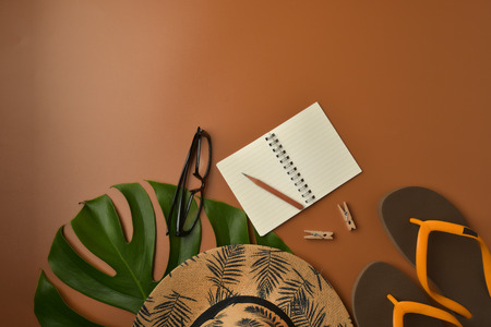 Flat lay, top view workspace with eye glasses, notebook, hat, pencil, green leaf, shoes and coffee cup on brown background. Summer stylish traveller blogger concept.の写真素材
