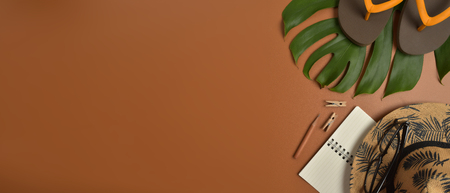 Flat lay, top view workspace with eye glasses, notebook, hat, pencil, green leaf, shoes and coffee cup on brown background. Summer stylish traveller blogger concept.の写真素材