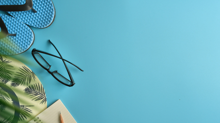 Flat lay, top view workspace with eye glasses, notebook, hat, pencil, green leaf, shoes and coffee cup on blue background. Summer stylish traveller blogger concept.の写真素材