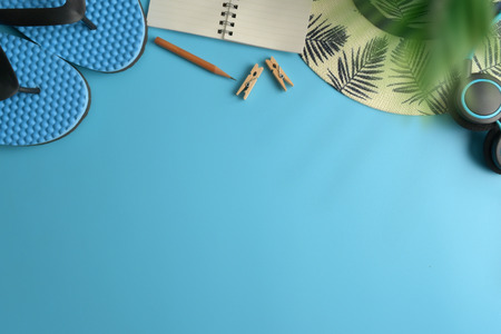 Flat lay, top view workspace with eye glasses, notebook, hat, pencil, green leaf, shoes and coffee cup on blue background. Summer stylish traveller blogger concept.の写真素材