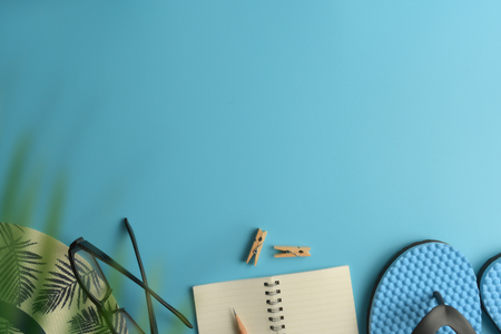 Flat lay, top view workspace with eye glasses, notebook, hat, pencil, green leaf, shoes and coffee cup on blue background. Summer stylish traveller blogger concept.の写真素材