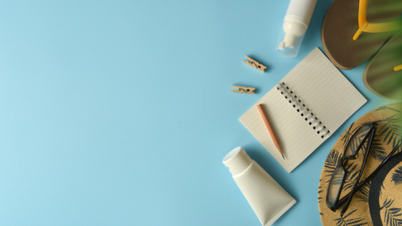 Flat lay, top view workspace with eye glasses, notebook, hat, sun block, shoes and coffee cup on blue background. Summer stylish traveller blogger concept.の写真素材