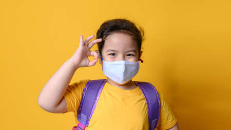 Little asian girl wearing mask for protect pm2.5 and Covid-19 with OK finger hands gesture . Covid-19 and Air pollution pm2.5 concept. E-learning or Home schooling education concept. New normal.Covid-19 coronavirus.の写真素材