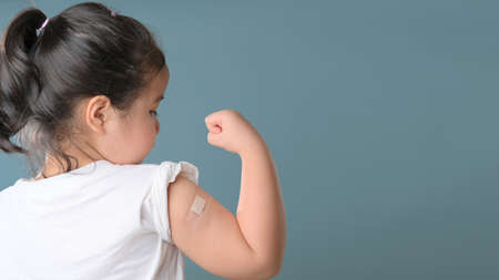 Little asian girl with bandage plaster on her arm after Covid-19 vaccination. Injection covid vaccine, healthcare for childrenの写真素材