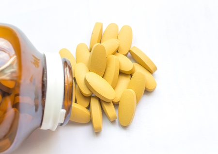 Yellow pills pouring out of the brown bottleの写真素材