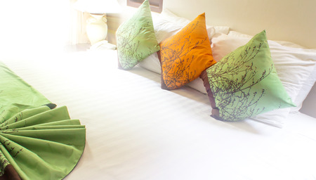 Three colorful striped pillows on white bed.の写真素材