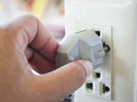 hand plugging in appliance to electrical outlet in wallの写真素材