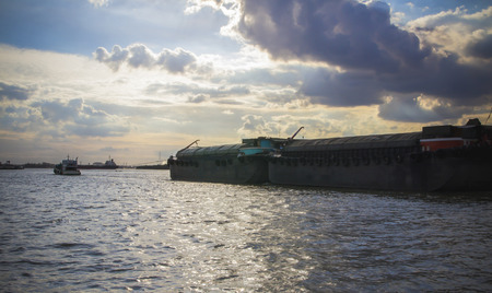 Tug boat drags barge on Chao Phraya river, Bangkok at sunset timeの写真素材