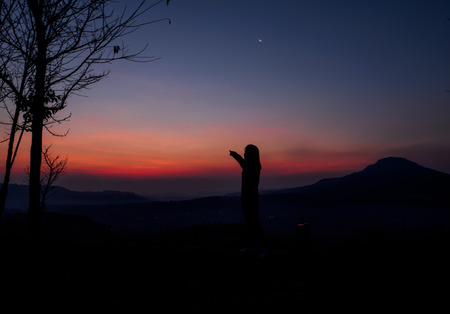 Silhouette of a woman standing over a view of the landscape in the sunriseの写真素材