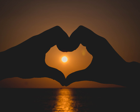 Silhouette hand in heart shape with sunset in the middleの写真素材