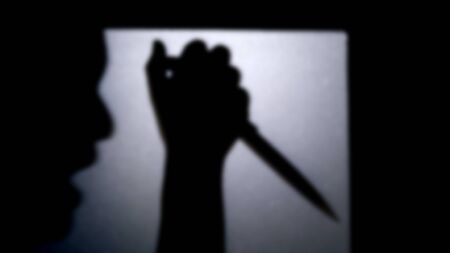 Blurred shadow of hand holding big sharp knife behind white mirror background. killer with...