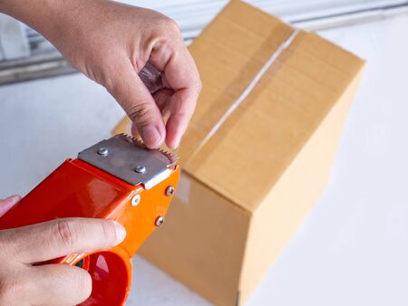 Hand holding roll of clear plastic packing tape and brown box isolated on white background.の写真素材