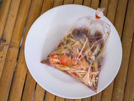 papaya salad in plastic bag on white dish and put on the wood tableの写真素材