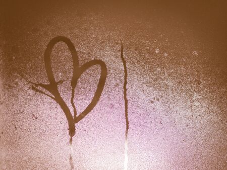 Broken heart shape drawn on window glass and water dropletsの写真素材