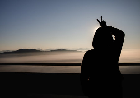 Silhouette of Happy woman showing two fingers while sunlight A symbol of peace and victory, or fighting.の写真素材