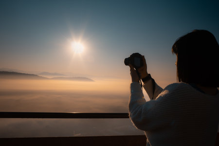 Young Asian woman take a photo at beautiful sunrise and colorful sky in the mist over the mountainの写真素材