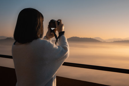 Young Asian woman take a photo at beautiful sunrise and colorful sky in the mist over the mountainの写真素材