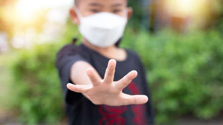 A 5 year old Asian boy wears a medicine healthcare mask and raises his hand. Do not approach. to maintain social distanceの写真素材