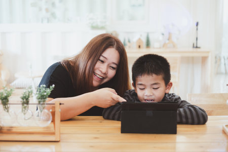 Mother Encouraging a five-year-old son While her son is studying online. Asian mother teaching his young son for lesson on E-learning classes in tablet at coffee cafe.The boy using tablet for learningの写真素材