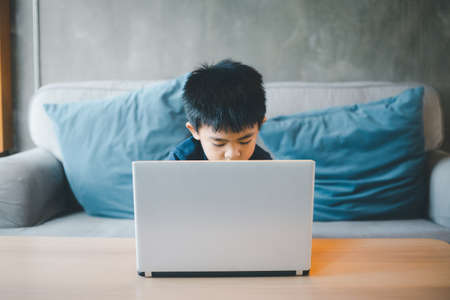 Four year old boy Asian man sits at a screen while studying at a coffee shop using his laptop to...