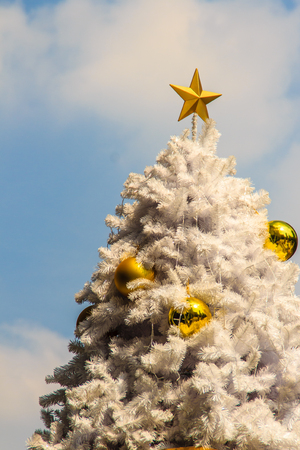 Beautiful Golden star on top of the outdoor white chrismas tree with golden balls recoration, cloud and blue sky backgroundの写真素材