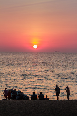 Beautiful sunset on the sea with orange, round and bright sun on the dusk over calm ocean in dramatic sky background. Silhouette people on foreground. View from Kamala beach, Phuket, Thailand.の写真素材