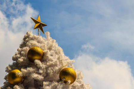 Beautiful Golden star on top of the outdoor white chrismas tree with golden balls recoration, cloud and blue sky backgroundの写真素材