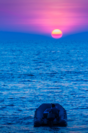 Beautiful sunset on the sea with orange, round and bright sun on the dusk over calm ocean in dramatic sky background. Silhouette boat and unidentified boat driver on foreground. View from Kamala beachの写真素材