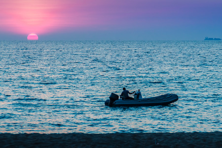 Beautiful sunset on the sea with orange, round and bright sun on the dusk over calm ocean in dramatic sky background. Silhouette boat and unidentified boat driver on foreground. View from Kamala beachの写真素材