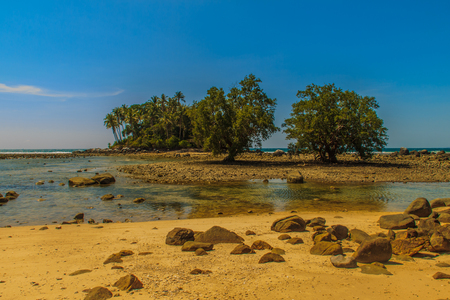 Lonely remote island with rock beach and tree when the sea water receded in blue sky and cloudy day backgroundの写真素材