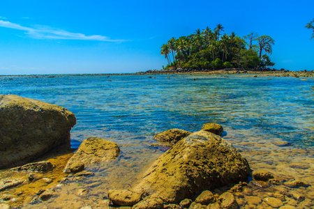 Lonely remote island with rock beach and tree when the sea water receded in blue sky and cloudy day backgroundの写真素材