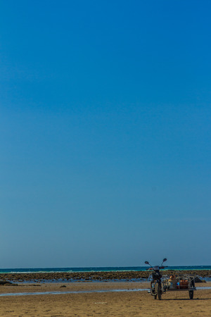 Fisherman was driving the motorcycle wagon to taken equipment to the boat in order to preparing his boat for the next fishing trip. His boat was park on the beach under blue sky and nearby the airportの写真素材