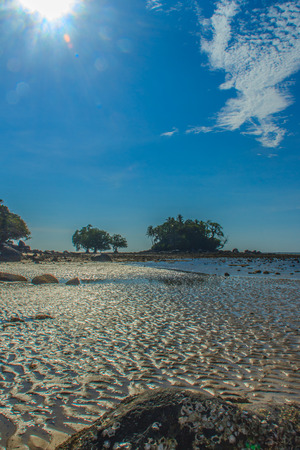 Lonely remote island with rock beach and tree when the sea water receded in blue sky and cloudy day backgroundの写真素材