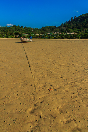 Traditional Thai wooden longtail boats (Rua Hang Yao) moored on the sand at small pier with blue sky and small island background in Phuket, Thailandの写真素材
