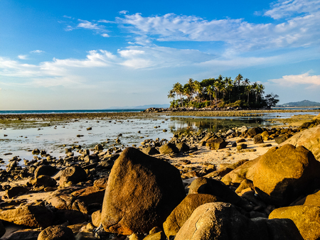 Lonely remote island with rock beach and tree when the sea water receded in blue sky and cloudy day backgroundの写真素材