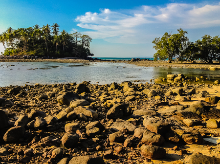 Lonely remote island with rock beach and tree when the sea water receded in blue sky and cloudy day backgroundの写真素材