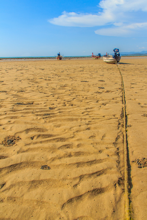 Traditional Thai wooden longtail boats (Rua Hang Yao) moored on the sand at small pier with blue sky and small island background in Phuket, Thailandの写真素材