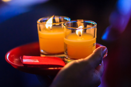 Poor light with noise grain of hand holding candles in the transparent glasses shining in the darkness as a symbol of contemplation, meditation and calmness. People praying for good luck and richness.の写真素材