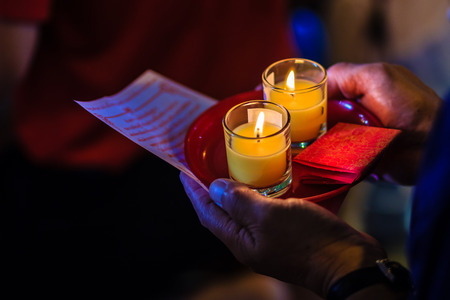 Poor light with noise grain of hand holding candles in the transparent glasses shining in the darkness as a symbol of contemplation, meditation and calmness. People praying for good luck and richness.の写真素材