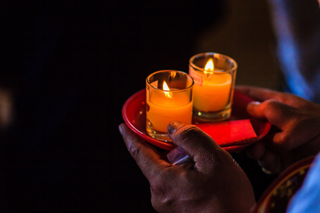 Poor light with noise grain of hand holding candles in the transparent glasses shining in the darkness as a symbol of contemplation, meditation and calmness. People praying for good luck and richness.の写真素材