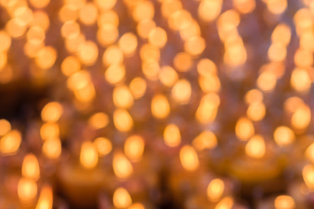 Beautiful blurred orange bokeh light of many candles, un-focus bokeh of the candle with dark background. Orange bokeh light of many candles in religious ceremonies. の写真素材