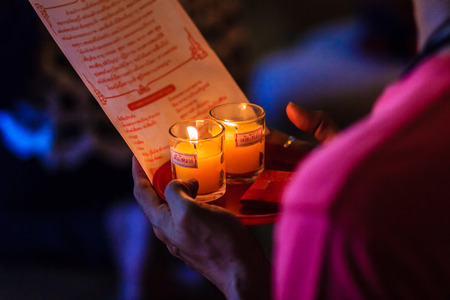 Poor light with noise grain of hand holding candles in the transparent glasses shining in the darkness as a symbol of contemplation, meditation and calmness. People praying for good luck and richness.の写真素材