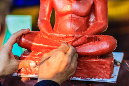 Sculptor carving the clay monk image. Thai sculpture artist molding and carving clay for making famous monk image. The craftsman concentrate to use the tools carving for art workの写真素材