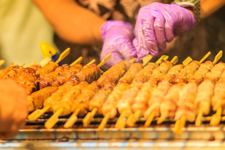 Close up the vendor grilling pork satay, Thai steak roasted pork grilling on the fire screen at night market in Bangkok, Thailand.の写真素材