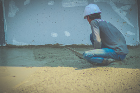 Masonry worker is using long trowel to smooth or leveling concrete flooring work step of the...