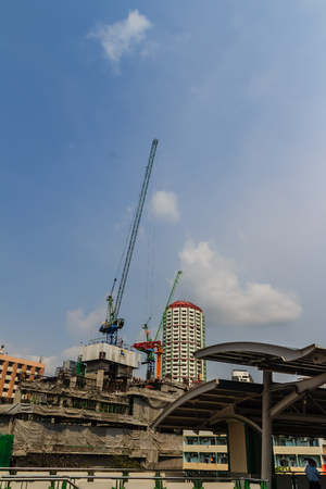View of luffing jib tower crane at condominium construction site over steel framework among high rise buildings in the center of Bangkok, Thailand.のeditorial素材
